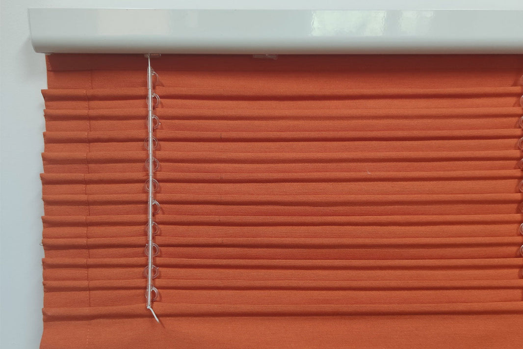 olidny biały mechanizm rolety rzymskiej z dystanserem widoczny z bliska, zamontowany na pomarańczowej tkaninie z precyzyjnym systemem sterowania koralikowego.