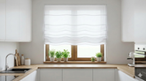 Jasna roleta rzymska zamontowana w nowoczesnej kuchni z drewnianym blatem i ziołami na parapecie.